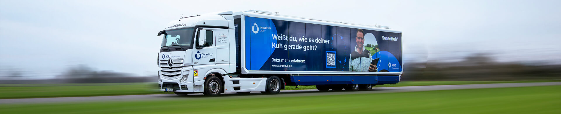 LKW, der auf einer Straße fährt, mit blauem Werbeplakat von SenseHub